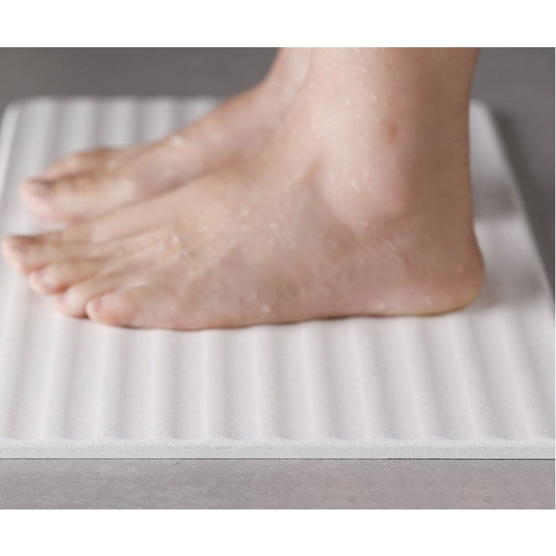 Wet bare feet standing on a ribbed white diatomite bath mat with visible water droplets